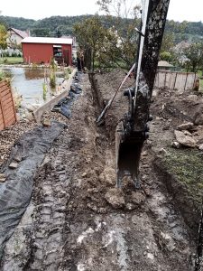 Minikotróval ásott keskeny árok kerti tó mellett
